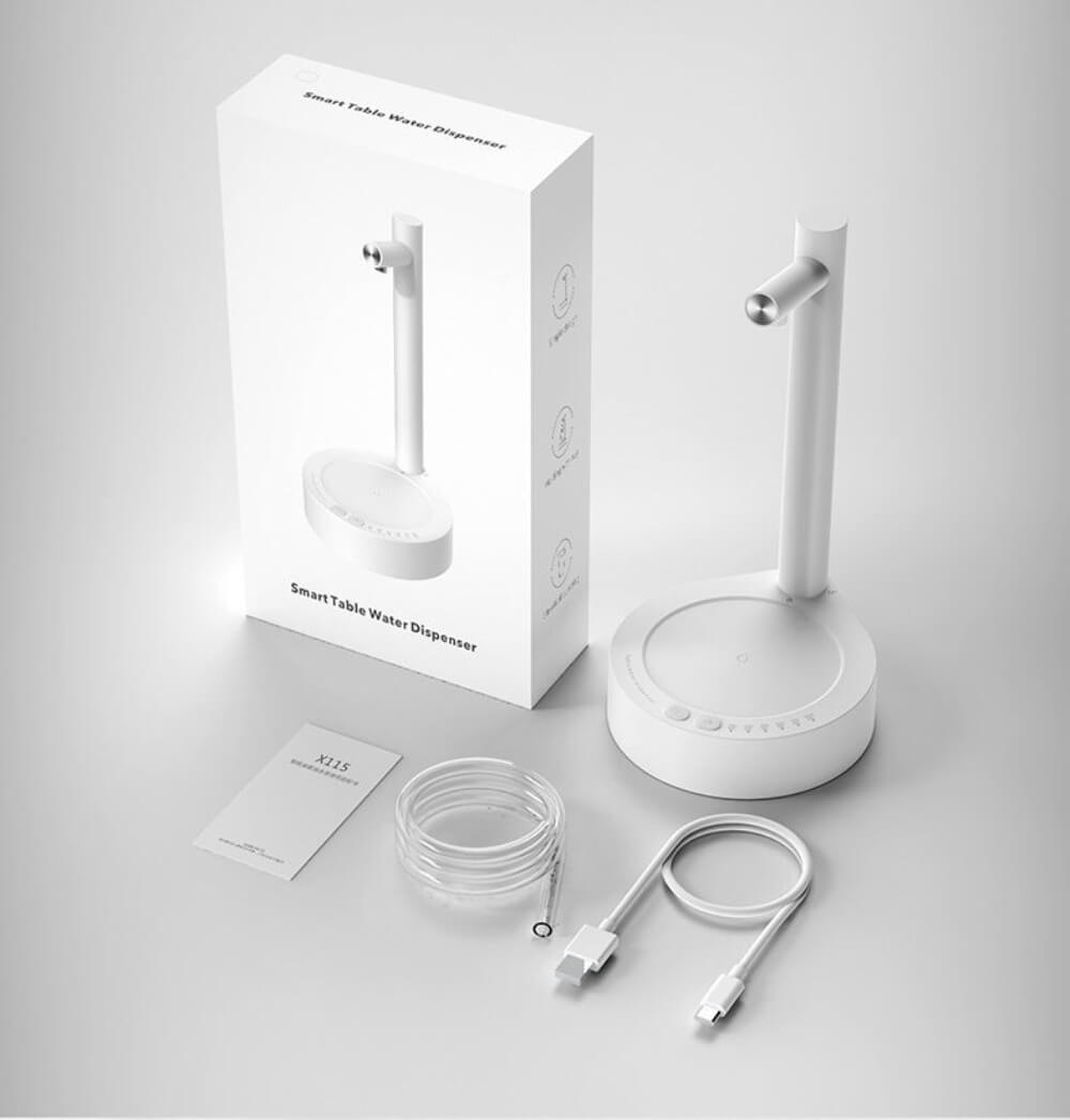 The mini water table dispenser in white, alongside its box packaging, its charging cable, water tube and manual.